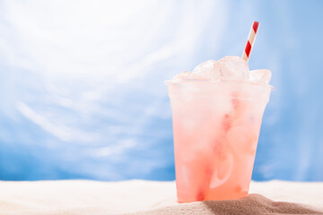 Fresh strawberry beverage with ice, straw in plastic glass on sandy tropical beach with sea view, copy space. Vacation, relax on coast.