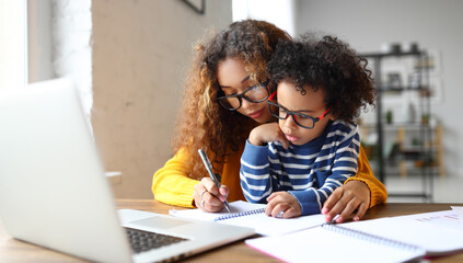 African mom taking care of little son, sitting together at desk and learning to write