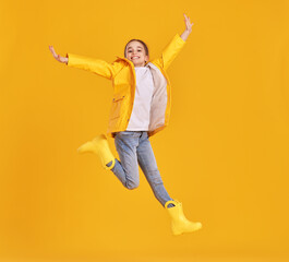 Jumping kid in raincoat and gumboots