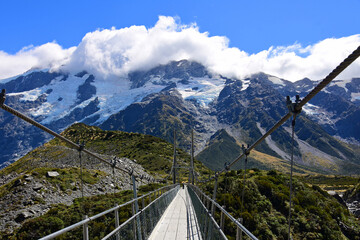 spectacular  mountain  scenery and a suspension bridge on the hooker river on a sunny day in summer along the hooker valley track near mount cook village on the south island of new zealand 