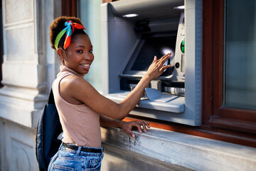 Beautiful african women using ATM machine. Attractive young woman withdrawing money from credit...