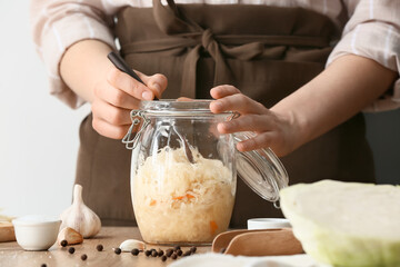 Woman preparing tasty sauerkraut at kitchen table, closeup