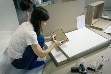 Millennial Woman unpacking boxes for assembling furniture. Self-assembly furniture and DIY concept