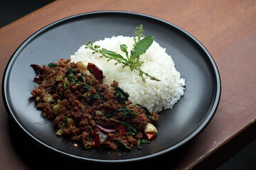 home made Thai's style spicy stir fried basil with minced beef served with Thai jasmine rice in black dish put on dark red wooden table with small free copy space on a side