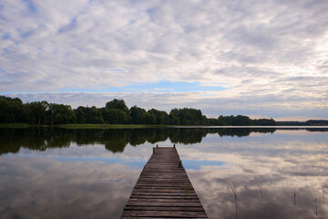 Fototapeta premium Wooden footbridge on the shore of the lake. Thick clouds above the lake