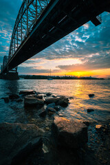 Beautiful sunset landscape with a bridge over river and stones in the water in the foreground. Dnipro River. Kyiv City. Ukraine.