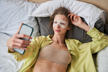 Woman wearing face mask smiling and looking at the smartphone while laying