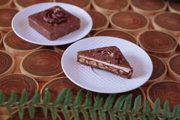 chocolate dessert with filling of caramel, nuts and nougats. The cake is covered with chocolate on a wooded background with a morning natural light