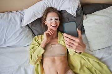 Woman wearing face mask smiling and looking at the smartphone while laying