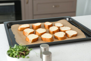 Baking sheet with slices of fresh bread on kitchen table