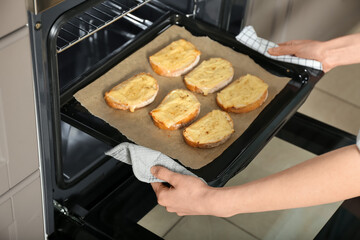 Woman taking baking sheet with toasted bread out of oven, closeup