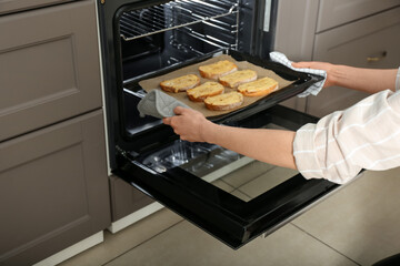 Woman taking baking sheet with toasted bread out of oven, closeup