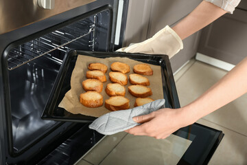 Woman taking baking sheet with toasted bread out of oven, closeup