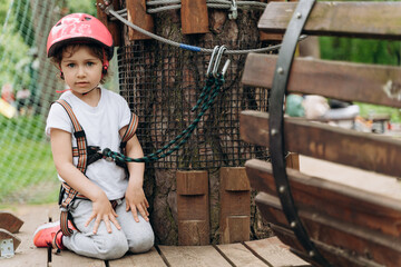 Small child in a rope park passes obstacles. Cute, beautiful girl in insurance and helmet