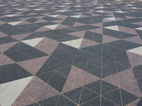 The square is paved with triangular tiles. Grey, white, black tiles on the street. The cobblestone surface. Modern design of streets, avenues, squares, shopping centers. Wear-resistant flooring