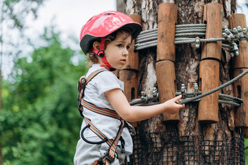 Cute, beautiful, little girl is actively spending time in the rope park. A child in a protective...