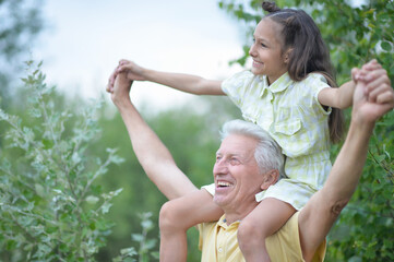 Obraz premium Portrait of happy grandfather and granddaughter having fun in park