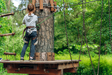 Girl on a suspended, wooden road prepares for a hike through obstacles. The child actively spends time