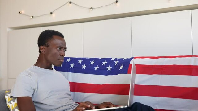 Young African-American guy sitting on the sofa at home exults for success after reading the good news.