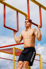 Fototapeta premium Athletic young man hanging from the bars at the calisthenics gym outdoors smiling