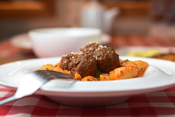 Macaroni dinner with meatballs. Meat pasta served in a white plate over red plaid tablecloth.