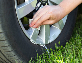 A man cleans the rims of a car from dirt and bitumen from the road using special wipes and a...