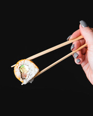 Hand holding sushi roll using chopsticks on black background. Cheddar cheese sushi roll over black