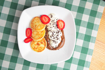 Cottage cheese pancakes, syrniki, ricotta fritters on ceramic plate with fresh strawberry.