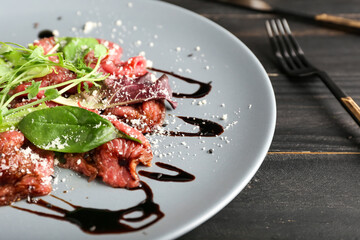 Plate with tasty veal carpaccio on dark wooden background, closeup