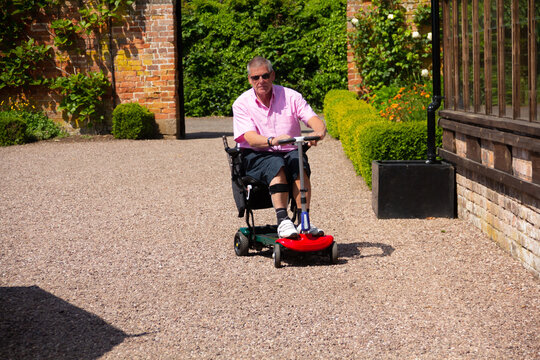 Male driving a mobility scooter on a summers day enabling him to enjoy the independence to be able to drive round and look at gardens in rural Shropshire despite his disability preventing him walking.