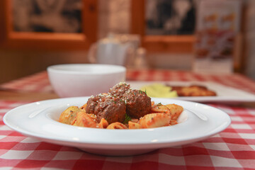 Macaroni dinner with meatballs. Meat pasta served in a white plate over red plaid tablecloth.