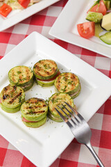 Appetizer from tomatoes, zucchini and mozzarella cheese served on a white plate with other dished on the table.
