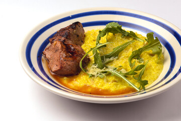 Risotto with meat steak and sauce served in a white plate over white backround.