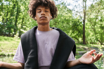 Fototapeta premium Man keeping eyes closed and meditating at the cozy forest or park