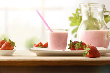 Glass and jug full of strawberry smoothie on wooden bench