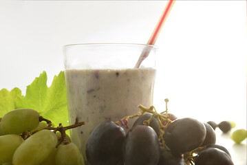 Glass with grape drink between bunches of red and white grapes