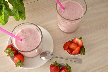 Two glasses of strawberry milkshake on wooden table elevated