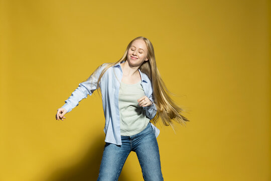 Portrait carefree young woman dancing on yellow background
