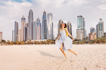 Funny woman in a sundress jumping with a background of huge skyscrapers in Dubai