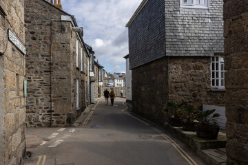 Fototapeta na wymiar A couple walk hand in hand through a narrow street of granite cottages in traditional fishing village of Mousehole, Cornwall
