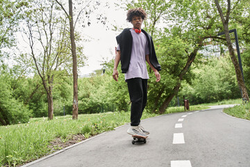Man with curly hair practicing skateboarding while enjoying active rest at the urban road