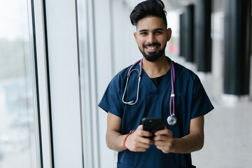 Young male doctor sit at desk in hospital consult client on modern smartphone online