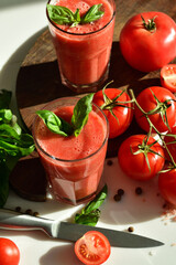 Two glasses of fresh organic tomato juice decorated with raw tomatoes and green leaves of basil on light background.Healthy diet nutrition concept.