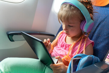 girl with headphones watching and listening in flight entertainment on board an airplane.