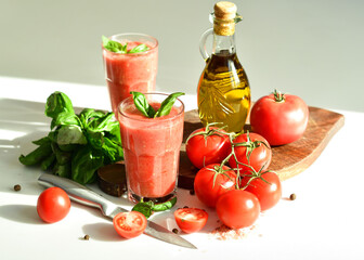 Two glasses of fresh organic tomato juice decorated with raw tomatoes and green leaves of basil on light background.Healthy diet nutrition concept.