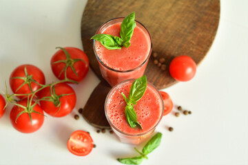 Two glasses of fresh organic tomato juice decorated with raw tomatoes and green leaves of basil on light background.Healthy diet nutrition concept.