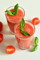 Two glasses of fresh organic tomato juice decorated with raw tomatoes and green leaves of basil on light background.Healthy diet nutrition concept.
