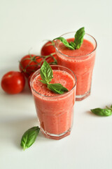 Two glasses of fresh organic tomato juice decorated with raw tomatoes and green leaves of basil on light background.Healthy diet nutrition concept.