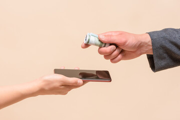 Buying a new smartphone concept. Female hand with a mobile phone and male hand gives a money to the...