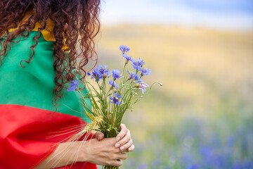 Woman covered with flag of Lithuania holding bouquet of blue cornflowers in a rye field. Lithuanian...